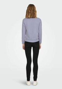 Felpa viola chiaro con scollatura rotonda e polsini aderenti, abbinata a jeans skinny neri e scarpe da ginnastica bianche.