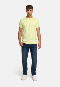 Helles gelbes T-Shirt mit kurzen Ärmeln und Rundhalsausschnitt; kombiniert mit dunkelblauen Jeans und weißen Sneakern. Verfügt über ein minimalistisches Design und eine bequeme Passform.