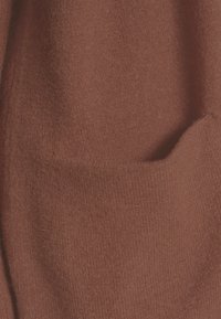 Tejido de color óxido con un acabado suave y texturizado. Presenta una costura de bolsillo visible, creando una apariencia de capas distintiva.