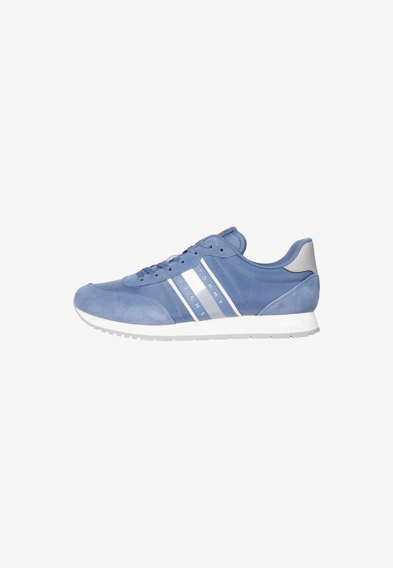 Zapatilla de ante azul con suela de goma blanca, que presenta tres rayas blancas y un logotipo en el lateral. Detalles en gris claro en el talón y la lengüeta.
