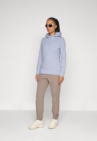 Lys blå langermet hettegenser med avslappet passform, kombinert med lysebrune tapered bukser og kremfargede joggesko.