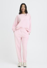 Roza trenirke in ustrezna oversize mikica iz mehke, strukturne tkanine. Ima rebraste manšete, elastični pas in stranske žepe.