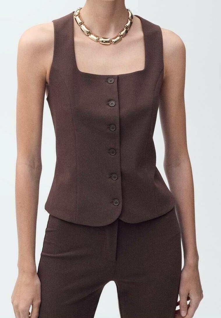 Gilet marron sans manches boutonné, assorti à un pantalon marron, complété par une grosse chaîne en or.