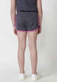 Pantaloni corti grigio scuro con rifiniture rosa, caratterizzati da un accento laterale e una vita elastica. Il modello indossa scarpe bianche. Vista da dietro.