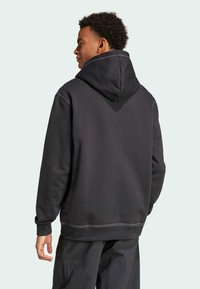 Zwarte hoodie met een grote capuchon, voorzien van contrasterende stiksels, een relaxte pasvorm en geribde manchetten, gedragen met donkere broeken.