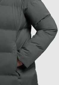 Giacca a vento grigia scura con un design trapuntato, dotata di un colletto alto, polsini elasticizzati e una tasca laterale con dettaglio a cordoncino.