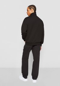 Black sweatshirt with high collar, paired with black cargo pants and white sneakers. Smooth texture, minimal design, and practical pockets.