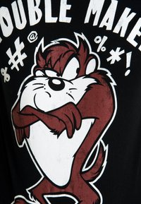 Black t-shirt featuring a cartoon character with a red and white color scheme, graphic design, and text "TROUBLE MAKER" in bold letters.
