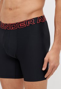 Čierne boxerky s červeným logom "UNDER ARMOUR" na elastickom pásiku, s priliehavým strihom a hladkým povrchom látky.
