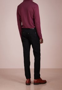 Bordeauxfarbenes Langarmoberteil, schwarze Jeans und braune Stiefel. Eng anliegend mit weicher Textur, hochgelegtem Kragen und minimaler Detailgestaltung.