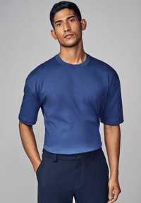 Marineblå kortærmet crew neck skjorte lavet af glat stof, med en afslappet pasform og subtil gradientstruktur, båret med mørke bukser.