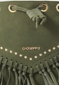 Borsa in suede verde oliva con hardware dorato, con dettagli in borchie e frange. Il nome del marchio "Gioseppo" è ben visibile.