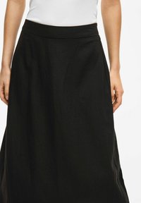 Jupe maxi noire avec une texture lisse, une taille large et des fentes sur les côtés. Fabriquée en tissu léger, offrant une silhouette fluide.