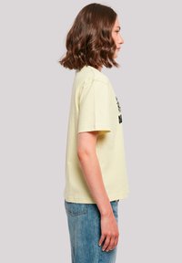 Light yellow cotton t-shirt featuring short sleeves and a relaxed fit. Front graphic in black adds contrast. Paired with high-waisted blue jeans.
