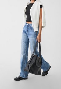 Mustat lyhyet paidat, valkoinen hihaton takki, vaaleansiniset levenevät farkut ja musta nahkalaukku. Sileät tekstuurit ja klassinen muotoilu.