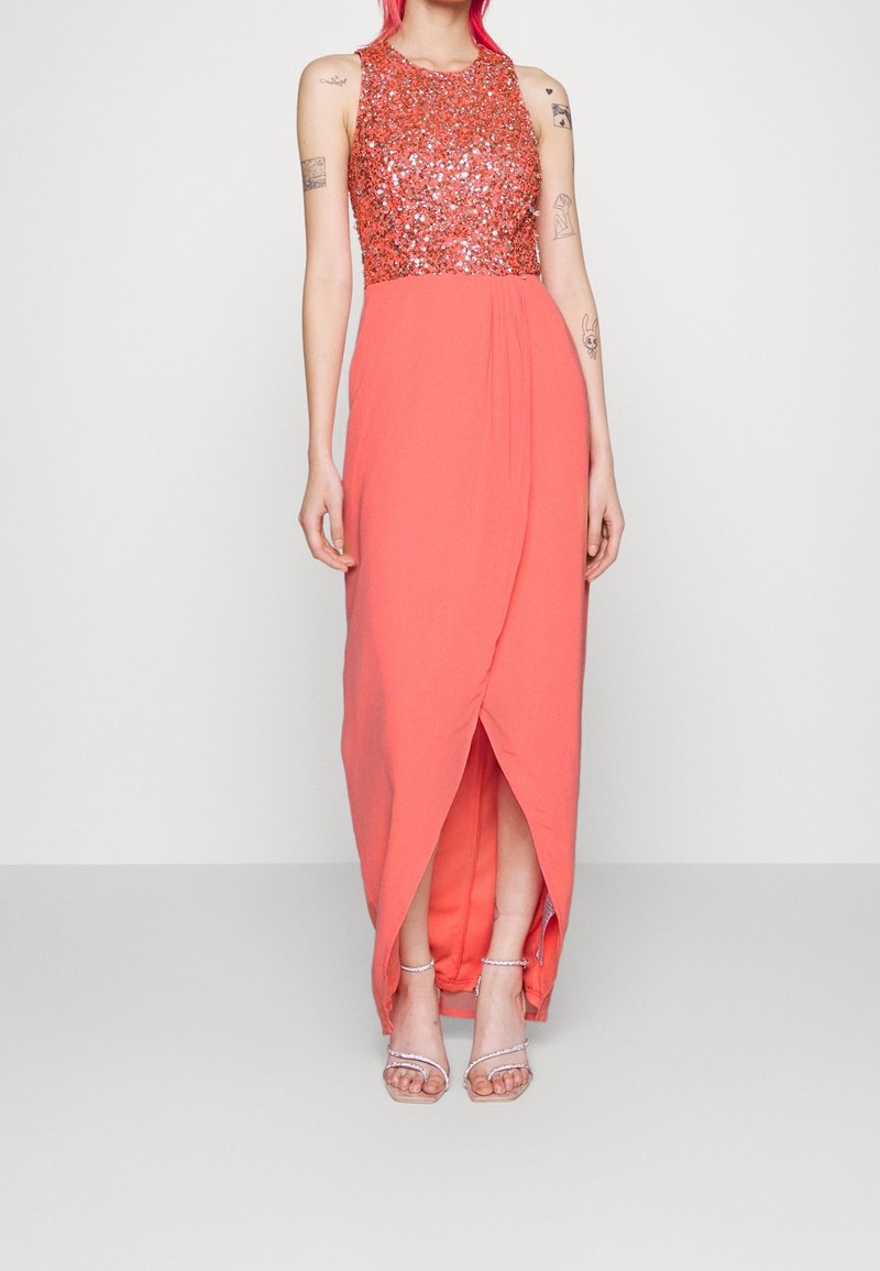Abito lungo corallo con corpetto in paillettes, design senza maniche e una fessura frontale. Presenta un tessuto morbido e una drappeggiatura sottile.