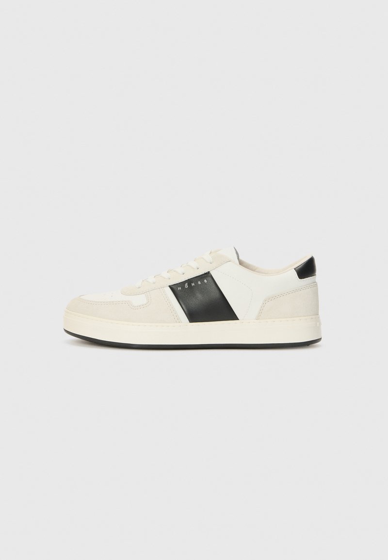 White and black sneaker with suede and leather upper, flat laces, rounded toe, and a textured sole. Features logo on the side.