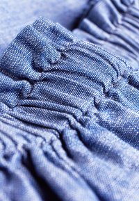 Tessuto blu raccolto con una superficie strutturata, caratterizzato da delicate macchie. Il tessuto mostra sfumature diverse e morbide pieghe.