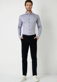 Hemd in Hellblau mit Muster und dunklen Knöpfen, kombiniert mit dunkelbraunen Cordhosen und weißen Sneakers, was einen lässigen Look ergibt.