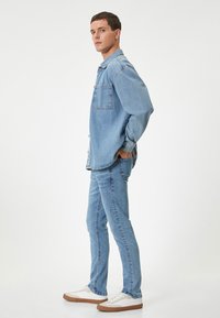 Camisa de mezclilla azul claro con un solo bolsillo, combinada con jeans azul claro a juego y zapatillas blancas con suelas marrones; ajuste casual.