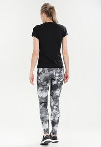 Svart kortärmad sporttopp kombinerad med grå leggings i figurnära modell med blommönster. Glansigt material med en jämn textur.