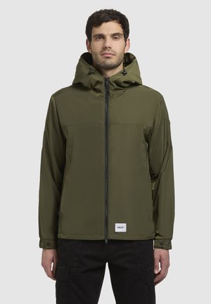 Olive green waterproof jacket with a zip front, adjustable hood, and black accents. Features a chest pocket and logo patch at the hem.