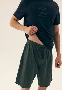 Ciemnoniebieska koszulka z centrowanym napisem, połączona z wzorzystymi zielonymi szortami z elastycznym pasem i sznurkiem.