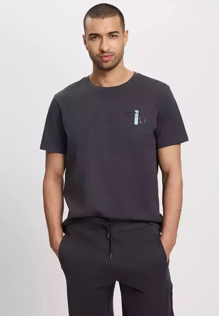 Czarnoszara bawełniana koszulka z krótkim rękawem, okrągłym dekoltem i jasnoniebieskim elementem graficznym na klatce piersiowej. W zestawie z ciemnymi dresami.