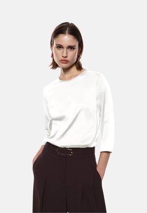 Top bianco in satin con scollatura rotonda e maniche a tre quarti, abbinato a pantaloni marroni a vita alta con dettaglio di fibbia argentata.
