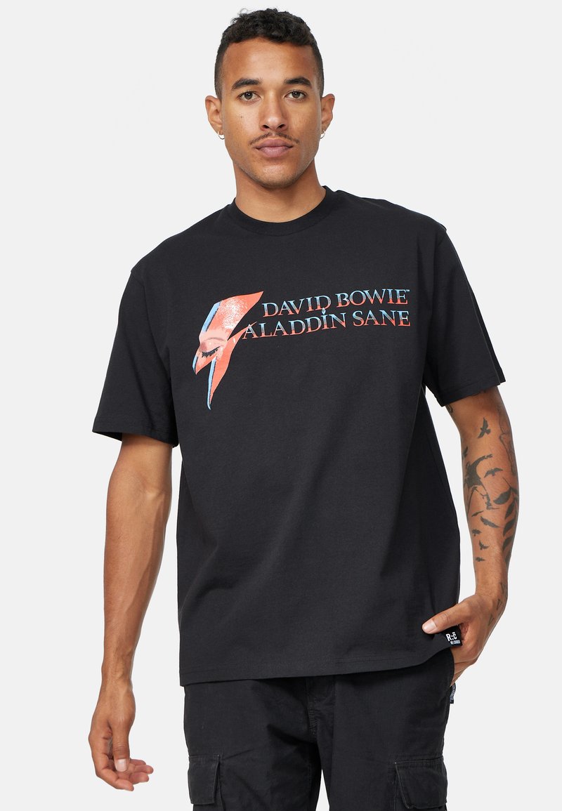Svart bomull t-shirt med texten "David Bowie Aladdin Sane" och en blixtgrafik i röd och blå. Loose fit med korta ärmar.