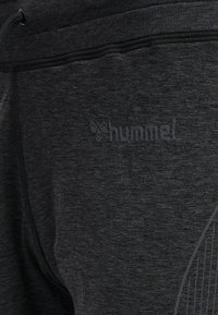 Svarta sport joggers i texturerat tyg med elastisk midja, med "hummel"-logotypen i en subtil, mörkare nyans på sidan.