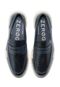 Marineblå loafers med vävd textur på framsidan, gummisulor med en beige kant och ett dekorativt band över midjan.