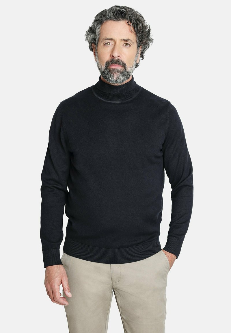 Suéter negro de cuello alto hecho de tela de punto acanalado, con mangas largas y un diseño ajustado, combinado con pantalones beige claros.