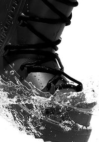 Bota negra impermeable con una superficie texturizada, sistema de cordones y una suela resistente, parcialmente sumergida en agua con salpicaduras.