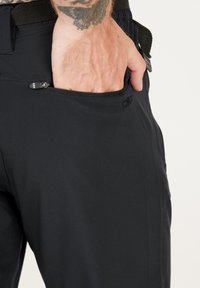 Svarta byxor i mjukt och stretchigt material med en ficka med dragkedja. Har en skräddarsydd passform och minimal märkning på midjebandet.