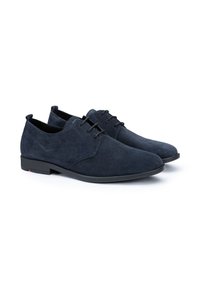 Chaussures en suède bleu marine avec une texture lisse, présentant un design classique à lacets et une semelle en caoutchouc. Inclut un accent subtil sur le talon.
