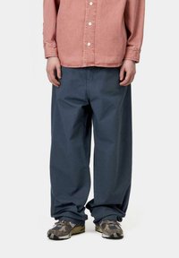 Pantalones de pierna ancha azul de algodón con una textura suave, que presentan un ajuste relajado y detalles de costura mínimos, combinados con zapatos marrones de estampado.