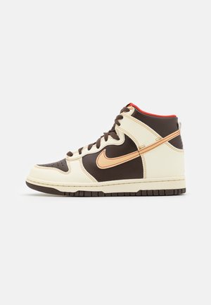 High-top sneakers featuring a cream and brown leather exterior, orange accents, perforated toe box, and contrasting sole.