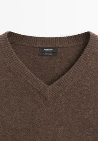 Pull en cachemire marron avec un design en V, présentant des poignets et un bas côtelés, et une étiquette indiquant 100% de matériau en cachemire.