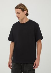 T-shirt nera a maniche corte in cotone, con scollo rotondo e vestibilità comoda. Il tessuto appare liscio e uniforme senza motivi.
