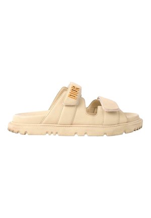 Sandale slide beige à bout ouvert avec deux brides réglables, semelle texturée et marquage "DIOR" sur la bride latérale.
