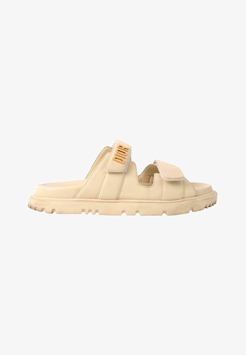Sandale slide beige à bout ouvert avec deux brides réglables, semelle texturée et marquage "DIOR" sur la bride latérale.