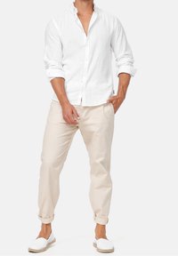 Weißes Leinenhemd mit Knöpfen und hochgekrempelten Ärmeln, kombiniert mit hellbeigen, schmal geschnittenen Hosen und weißen Slippern. Minimalistisches Design.