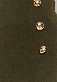 Tissu texturé vert foncé avec trois boutons ronds dorés brillants alignés verticalement.