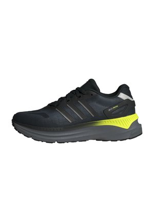 Chaussure de sport noire avec un dessus texturé, trois bandes argentées, des accents réfléchissants et un détail de semelle jaune vif. Semelle en caoutchouc.