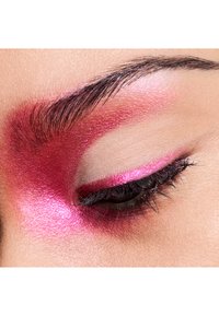 Lyserød øjenskygge med en shimmertekstur, kraftigt påført omkring øjenbrynet og øjenlåget, der fremhæver mørke øjenvipper.