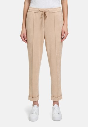 Beige suede jogger pants with a drawstring waist, front pleats, and cuffed hems. Paired with white sneakers for a casual look.
