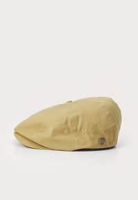 Lichtgele platte pet van zacht materiaal, met een ronde vorm, knoopaccenten en een klein logo-tag aan de zijkant.