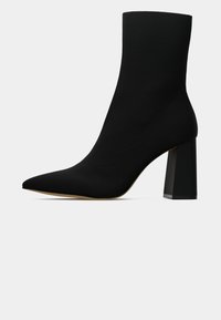 Stivale alla caviglia nero a punta con design tipo calza, caratterizzato da un tacco bloccato spesso e una texture di stoffa liscia.