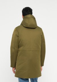 Olivgrüne, kapuzenjacke mit glatter, matter Oberfläche, geradem Schnitt und minimalistischem Design. Sichtbare Nähte und Logos auf dem Ärmel.